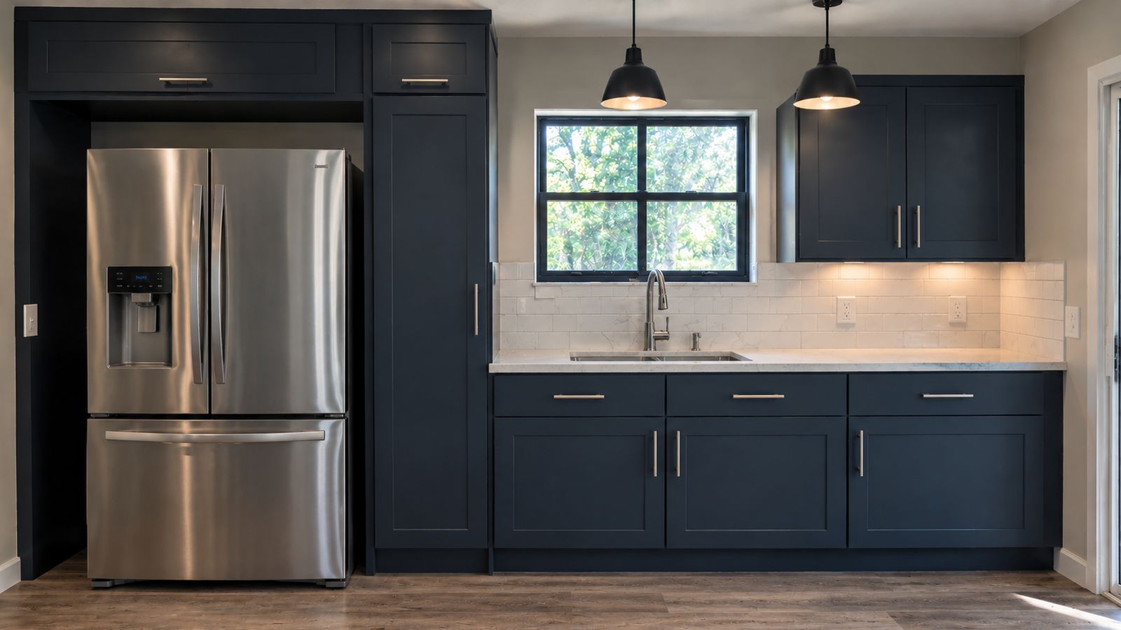 The same kitchen after: navy shaker cabinets, a built-in fridge surround, white subway tile, light quartz tops and new plank flooring